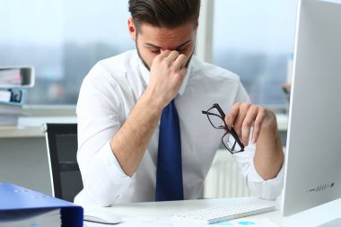 Masaüstünde gözlük tutan meşgul bir adam.