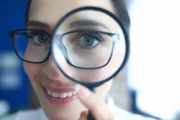 Woman with glasses looks through magnifier and smiles. — Stock Photo, Image