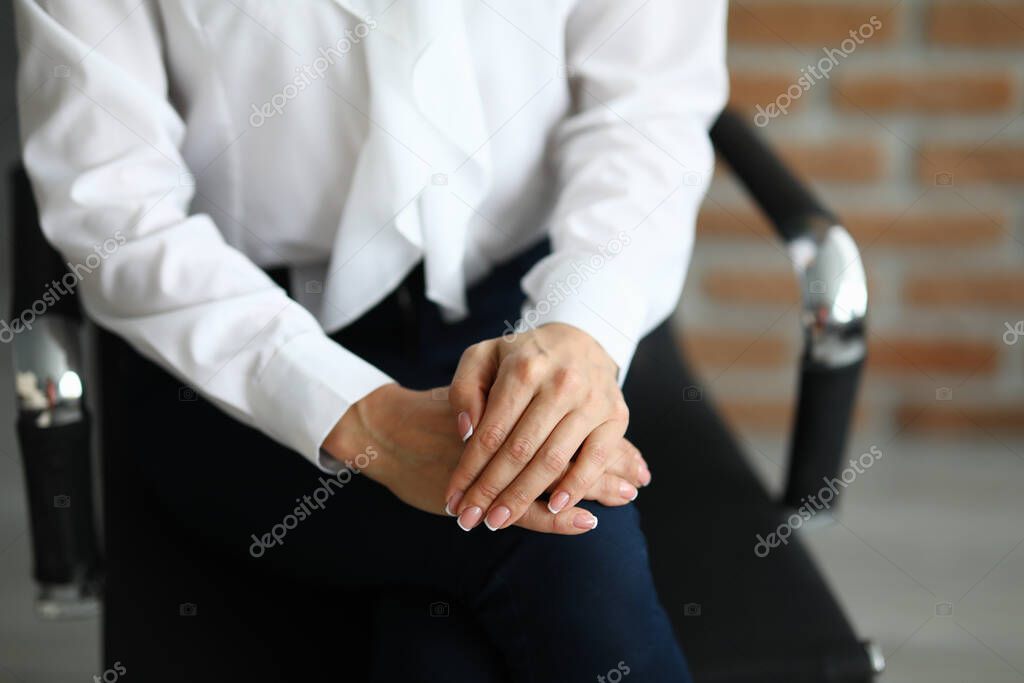 Woman sits on chair with hands clasped.