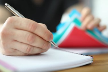 Adam kalemi elinde tutuyor ve deftere yazıyor.