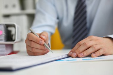 Ofiste kalemle kağıt işi yapan bir erkek.