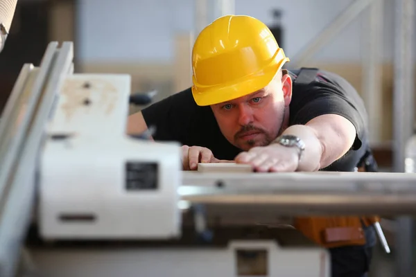 Man i gul hjälm med elektrisk såg i verkstad — Stockfoto