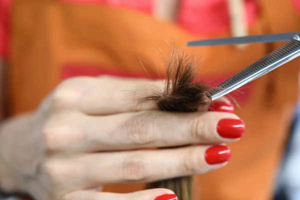 Weibliche Hand mit rotem Maniküre-Schnitt Haarsträhne Nahaufnahme mit Schere. — Stockfoto