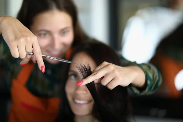 Bella donna in grembiule tenere le forbici in mano e tagliare i capelli del cliente primo piano. — Foto Stock