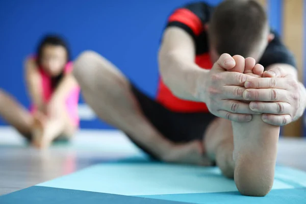 Mężczyzna siedzi na dywanie na siłowni i rozciąga swoje ciało z bliska. — Zdjęcie stockowe