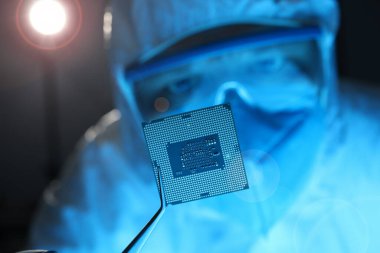 Maskeli adam ve gözlüklü adam elektronik çipi forseps ile yakın çekimde tutuyor.