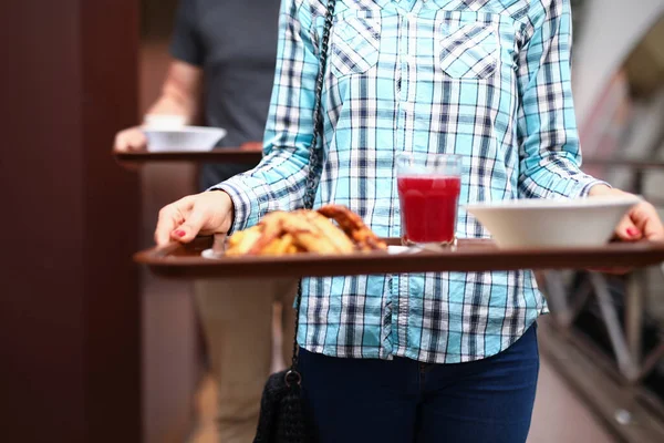 Woman stand in line with tray of food in her hands in a self-service restaurant.