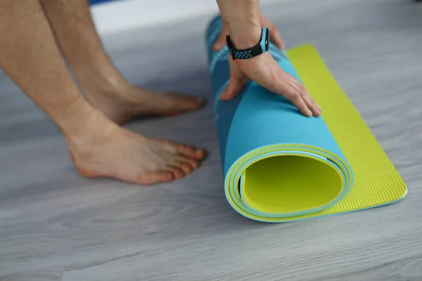 Man staan op vloer en rol multi-gekleurde gymnastiek tapijt op met zijn handen. — Stockfoto