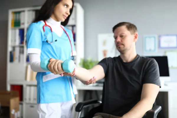 Žena v lékařském obleku a červený stetoskop vyšetřují návštěvníka ruku na zlomeninu. — Stock fotografie