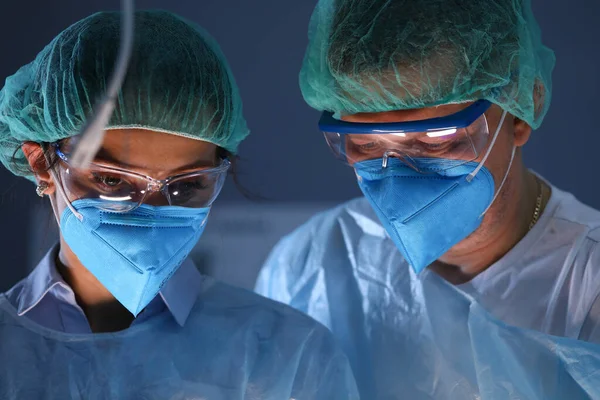 Man en vrouw in operatiepakken en masker staan zij aan zij en kijken toe. — Stockfoto