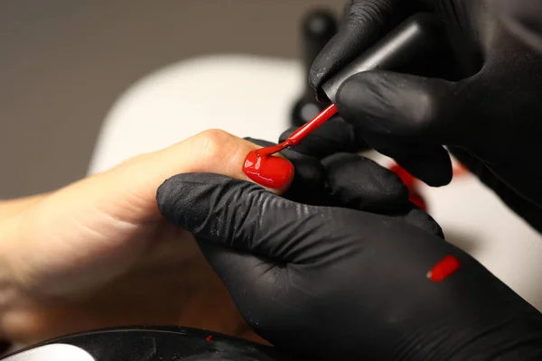 Ręce w czarnych rękawiczkach nakładają czerwony lakier — Zdjęcie stockowe