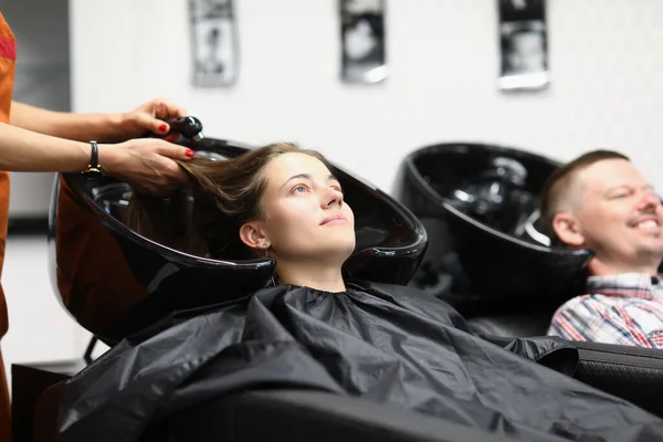 A salon employee washes hair to woman in the sink