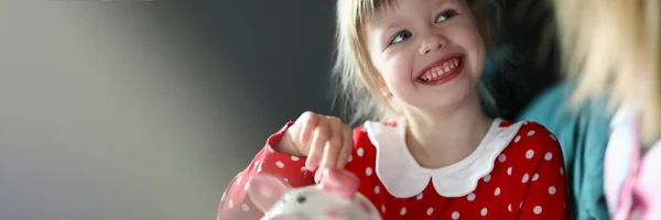 Gelukkig klein meisje in rode jurk houden zilveren munt in de hand — Stockfoto