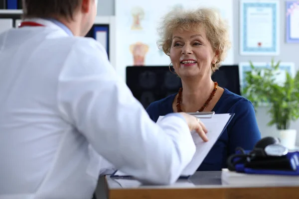 The doctor holds a folder and listens to a lady