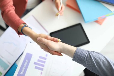 Bir kadın masanın üstünde bir erkekle tokalaşıyor.