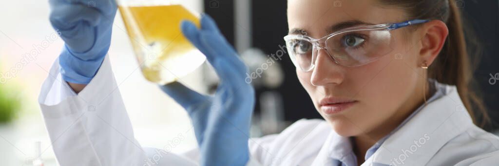 Chemist girl looks at flask with yellow liquid