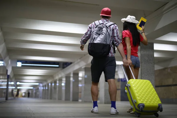 Couple stand with their backs and hold yellow suitcase by handle in underground passage. — Stock Photo, Image