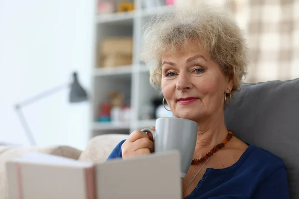 Grand-mère boire du café et lire le livre dans l'appartement. — Photo