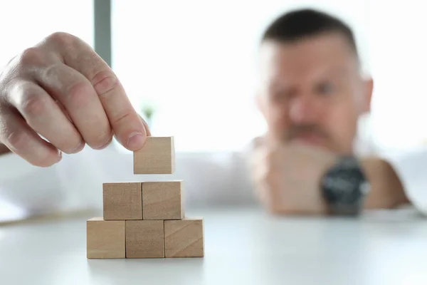 Geschäftsmann hält Holzwürfel in der Hand und baut Pyramide. — Stockfoto