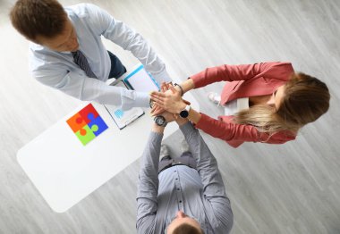 Ofiste iki erkek ve bir kadın el ele tutuşuyor..