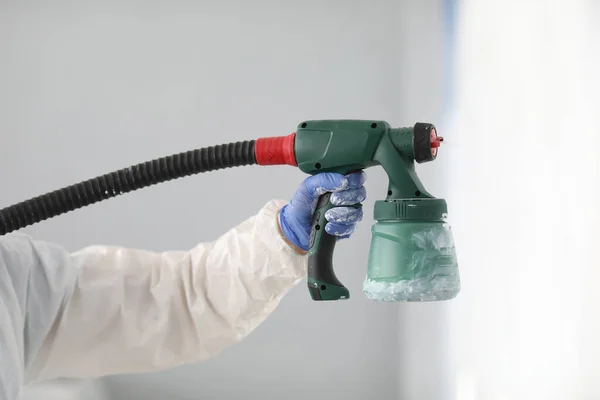 Mano masculina en traje protector mantenga pistola de spray en su mano de cerca. — Foto de Stock