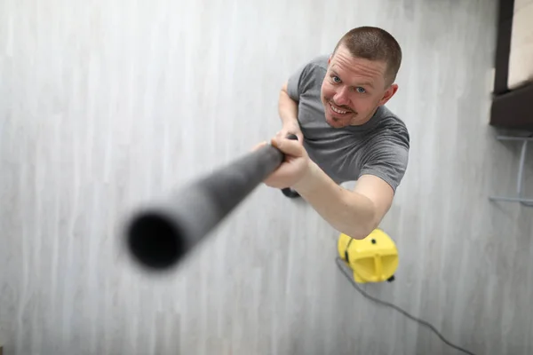 L'homme tient le tuyau noir de l'aspirateur jaune dans sa main et le soulève. — Photo