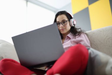 Gözlüklü kadın, kulaklıklı koltukta oturur ve dizüstü bilgisayar ekranına bakar.