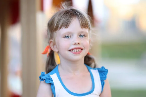 Portrét holčičky s modrýma očima na pozadí hřiště — Stock fotografie