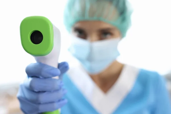 Жінка-лікар в захисній масці і рукавичках тримає термометр в руках для вимірювання температури тіла — стокове фото