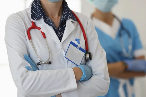Twee artsen in handschoenen en witte jassen staan met gevouwen armen — Stockfoto