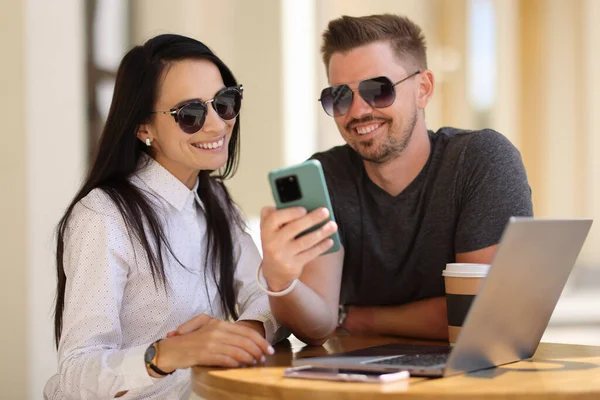 Leende man och kvinna sitter vid bordet och tittar in i smartphone — Stockfoto