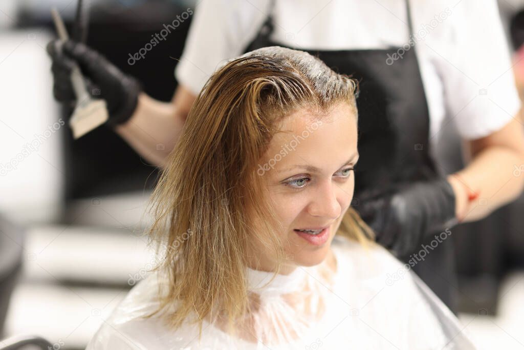 Woman in chair in hairdresser dyes her hair.