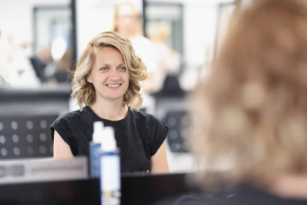 Mulher com um penteado à noite em um salão de beleza se senta na frente do espelho e sorri — Fotografia de Stock