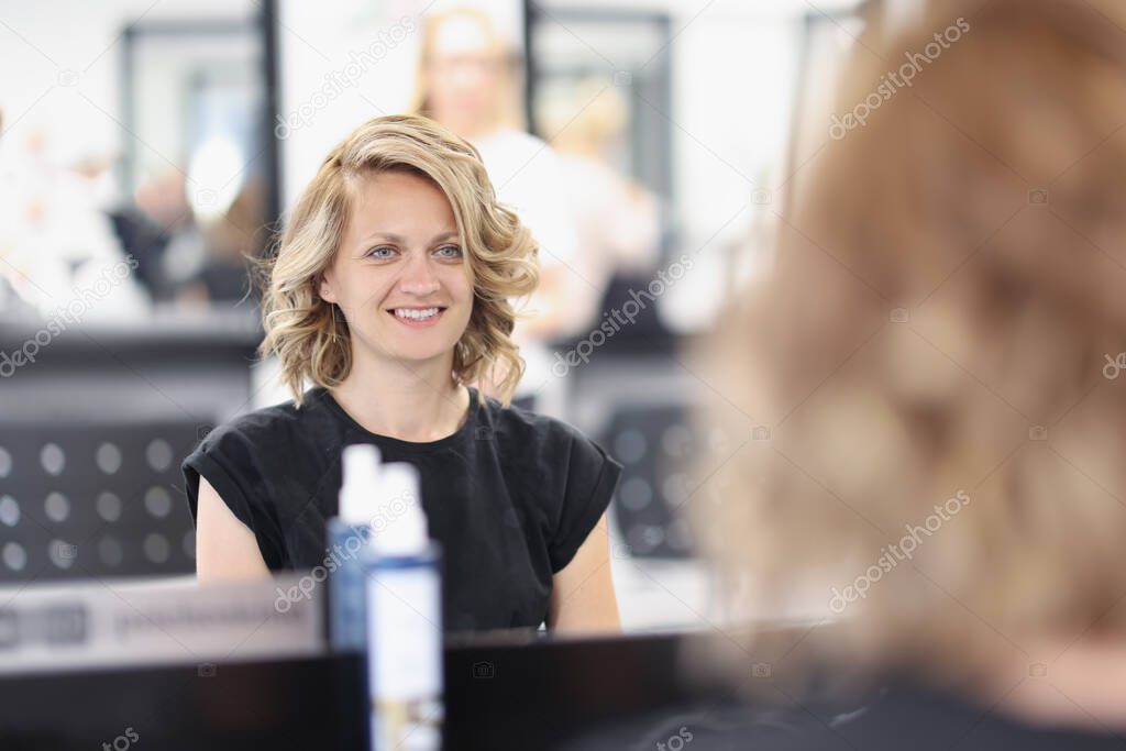Woman with an evening hairstyle in a beauty salon sits in front of mirror and smiles