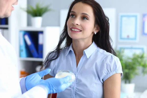 Femme en consultation avec un chirurgien plasticien tenant un implant dans sa main — Photo