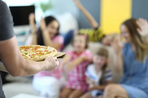 Çocuk ve yetişkinlerin neşeli geçmişine karşı elinde pizza tutan bir adam.. — Stok fotoğraf