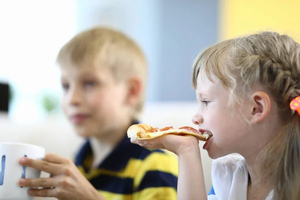 Little girl bites piece of pizza boy holding a cup. — Stock Photo, Image