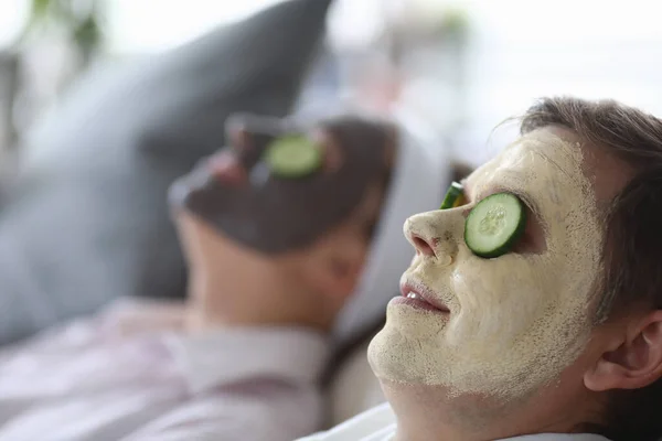 A máscara cosmética aplicou-se a caras masculinas e femininas e partes de pepino em olhos. — Fotografia de Stock