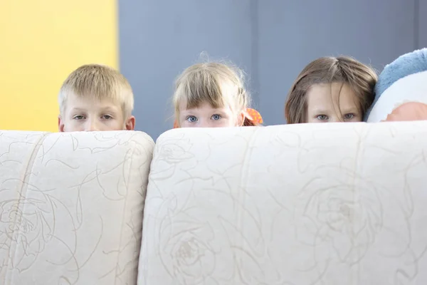 Ragazzo e due ragazze si nascondono dietro il divano e guardare fuori. — Foto Stock