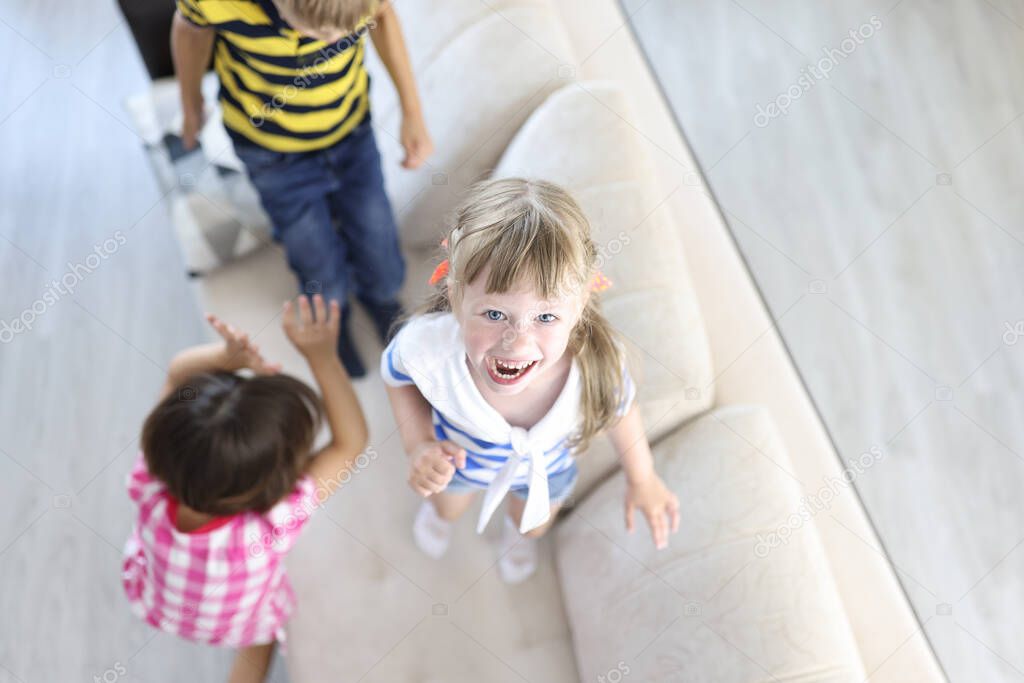 Boy and girls laugh and jump on couch at home.
