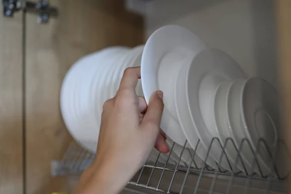 Frauenhand zieht sauberes weißes Geschirr aus Küchenschrank. — Stockfoto