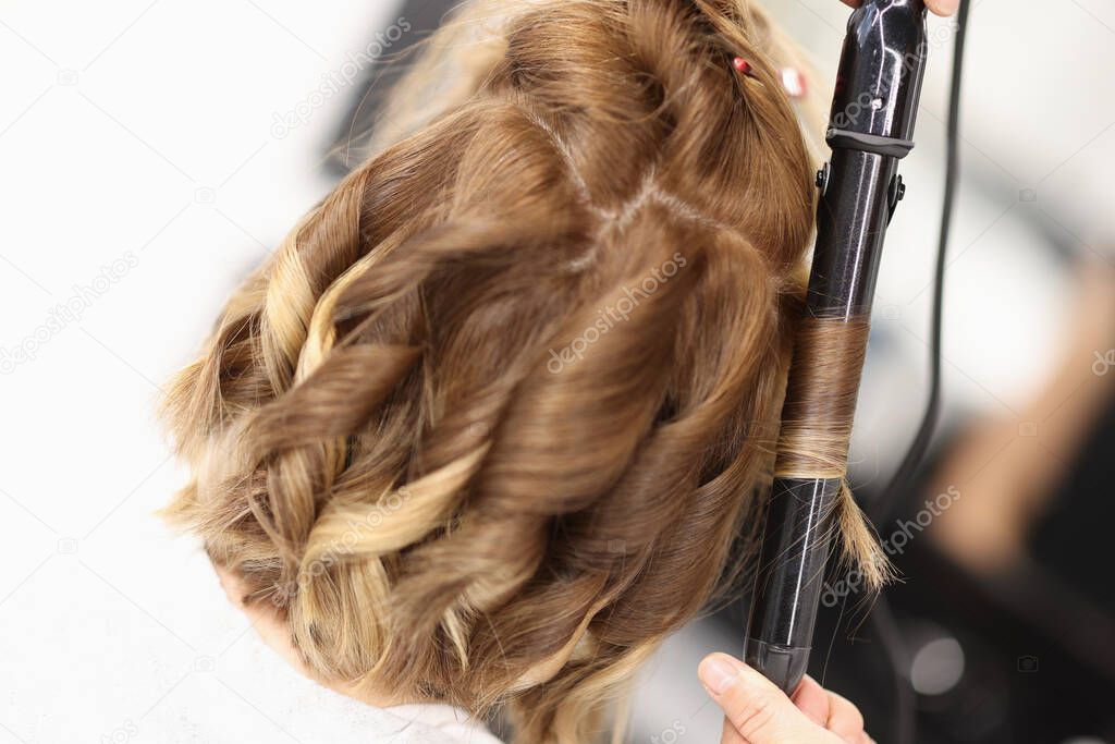 Hairdresser makes curls on womens hair with curling iron