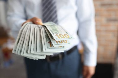 Adamın elinde 100 dolarlık banknot yelpazesi var.