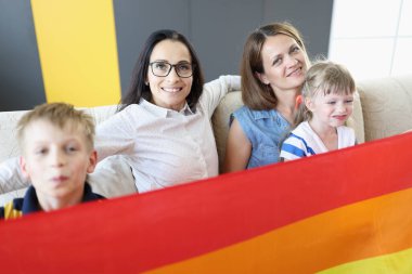 İki kadın, erkek ve bir kız LGBT bayrağının üstünde oturuyorlar..