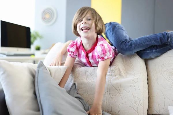 Girl and boy play around on couch at home and laugh.