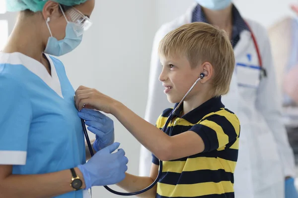 Мальчик в медицинском кабинете слушает, как врачи дышат через стетоскоп — стоковое фото