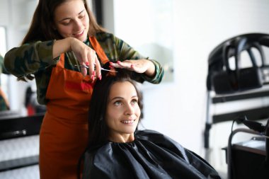 Önlüklü neşeli kadın kuaför kısa süre sonra makasla ziyaretçiye saç kesecek..