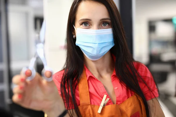 Woman hairdresser in medical mask holds scissors in hand