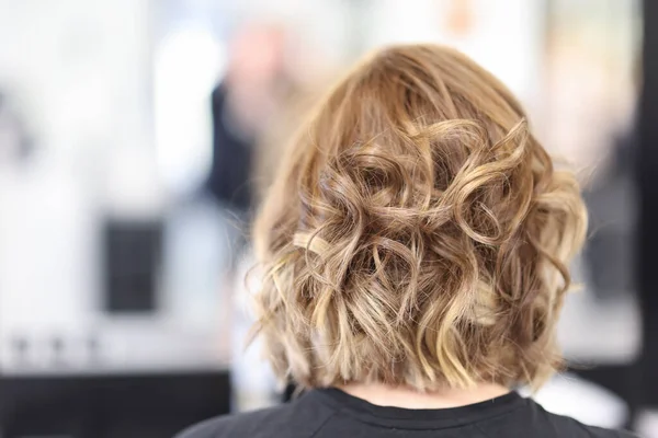 Femme aux cheveux bouclés assis dans le salon de beauté vue arrière. — Photo