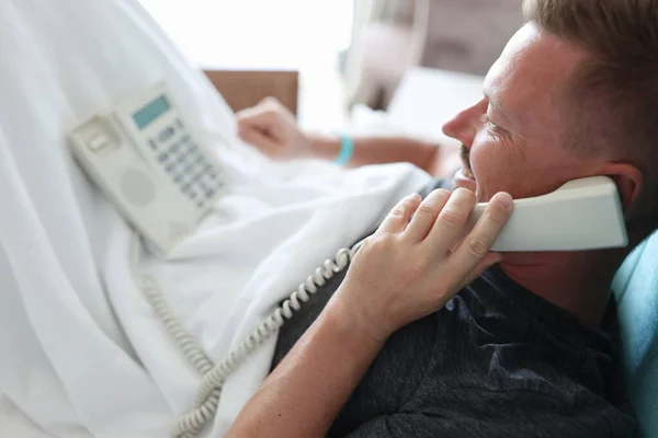침대에 누워 무릎을 꿇고 도시의 전화를 들고 있는 남자. — 스톡 사진